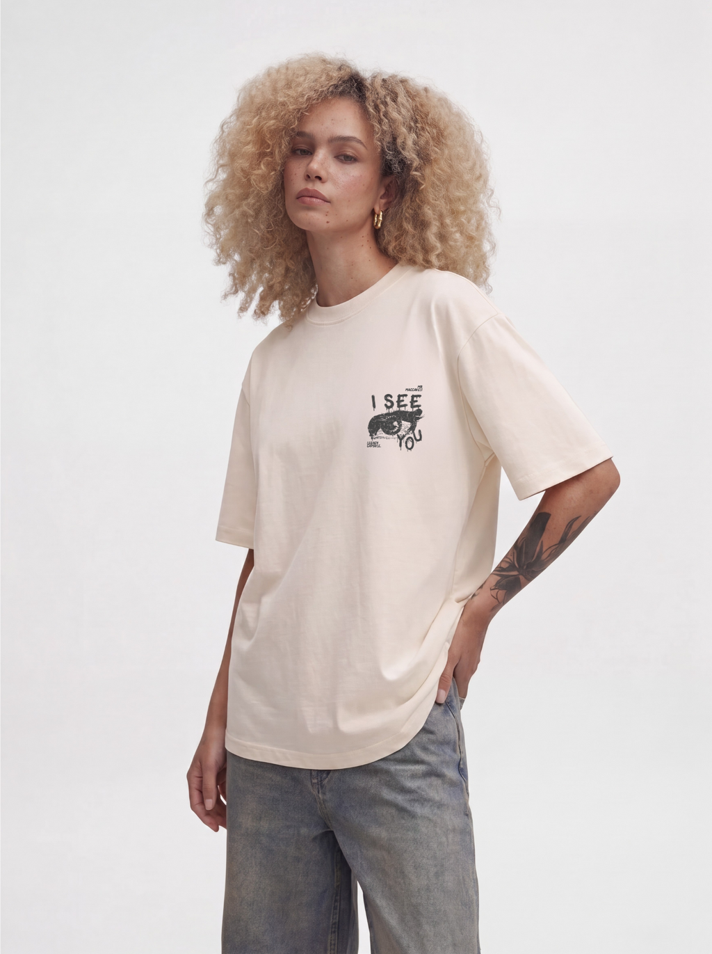 Person wearing a beige t-shirt with a graphic design on a plain background